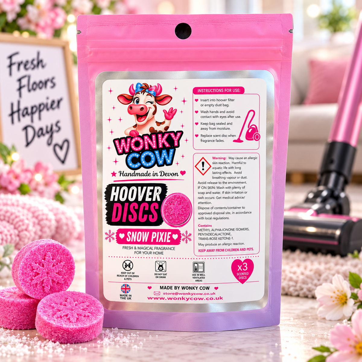 Wonky Cow Hoover Discs Snow Pixie pink reusable tampon packaging pouch, shown with three actual pink reusable tampons on a styled tabletop with flowers and a sign.