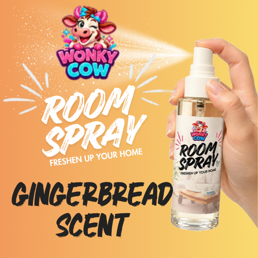 A hand holds a Wonky Cow Room Spray bottle with a white spray nozzle, shown releasing a mist against a warm yellow-orange gradient background with large text reading 'ROOM SPRAY' and 'GINGERBREAD SCENT'.