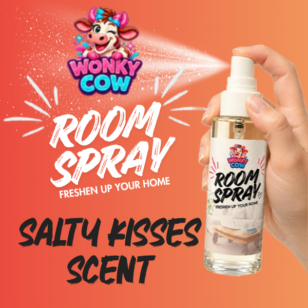 A hand holding a Wonky Cow Room Spray bottle labeled 'Salty Kisses Scent' against a bright orange background with product text and a cartoon cow logo.