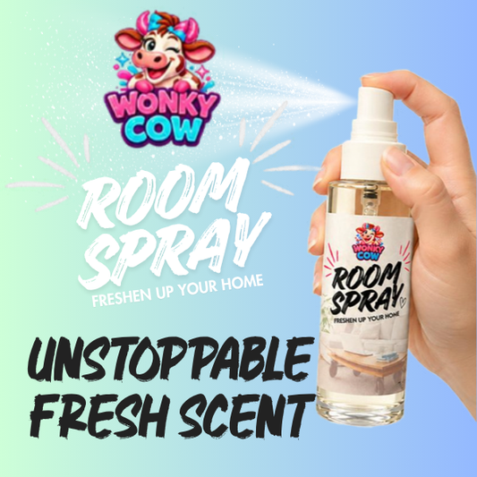 A hand holds a clear room spray bottle labeled Wonky Cow Room Spray against a light blue gradient background with promotional text reading 'ROOM SPRAY' and 'UNSTOPPABLE FRESH SCENT.' The bottle is transparent with a white spray top and a mostly white label featuring pink and blue branding.