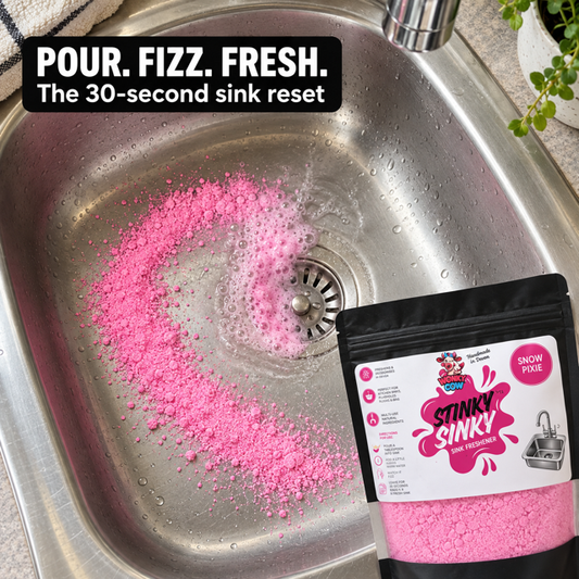 Pink powder sink reset being poured into a stainless steel sink with running water, alongside a black resealable pouch labeled Stinky Sinky Snow Flake.